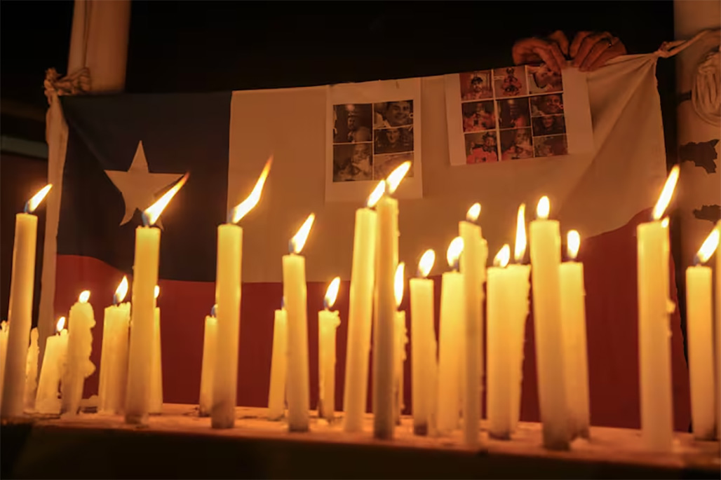 Velas encendidas durante una vigilia con la bandera chilena de fondo y las víctimas de un derrumbe minero, frente a la mina de cobre El Teniente, operada por Codelco, donde un derrumbe mató a un trabajador y atrapó a otros cinco bajo tierra, deteniendo las operaciones en Rancagua, Chile, el sábado 2 de agosto de 2025.